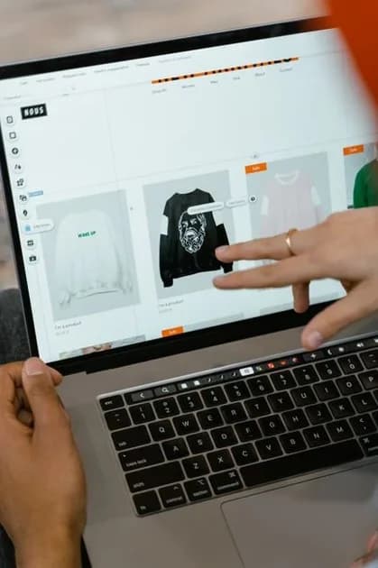 Close-up of a person's hands using a laptop displaying an online shopping page in a bright indoor setting