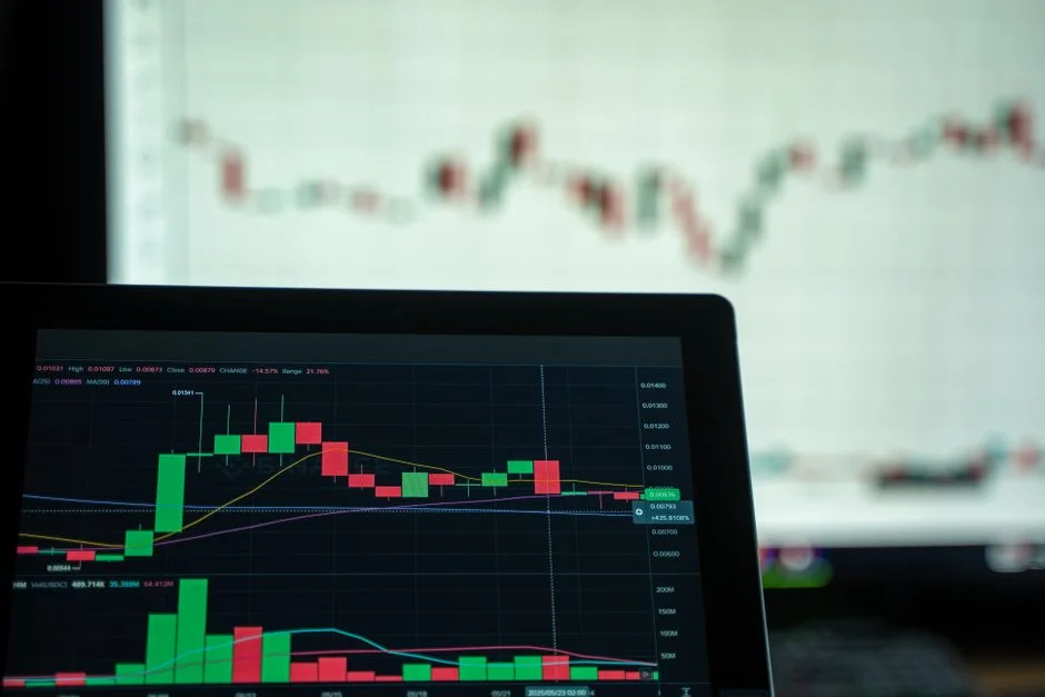 Close-up of a laptop screen displaying a detailed candlestick trading chart with green and red price bars, financial ana