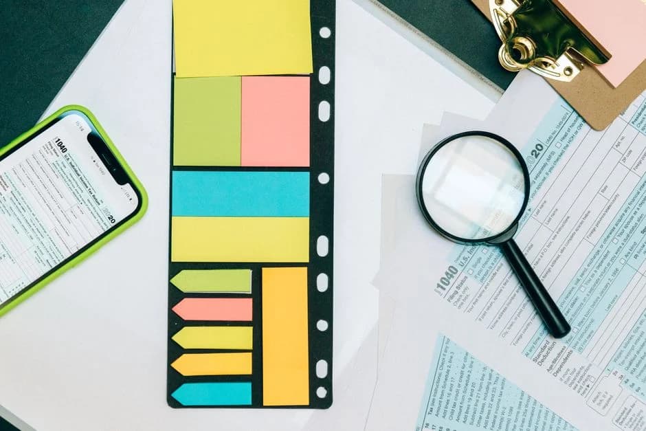 Colorful office supplies arranged on tax documents with a smartphone and magnifying glass nearby