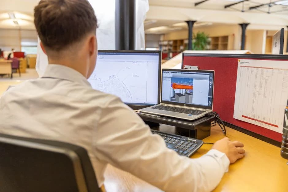Back view of an engineer working at dual monitors in a bright office