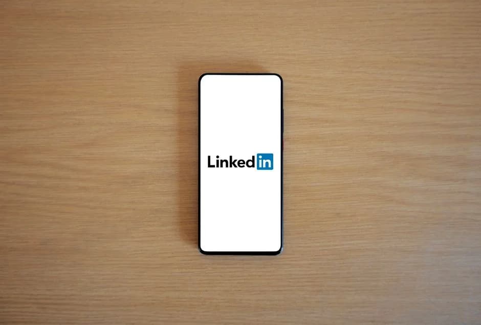 {'answer': 'A smartphone viewed from above, its screen showing the LinkedIn logo, resting on a wooden surface.'}