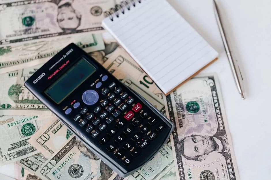 Calculator, notepad, and cash spread on a desk for budgeting outbound infrastructure costs in a B2B business setting.