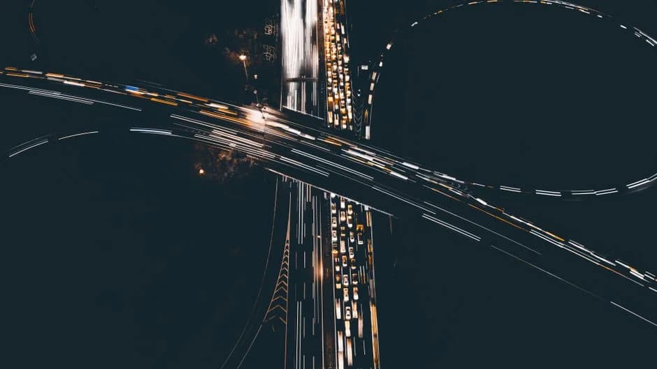 Aerial night shot of a busy highway interchange, with light trails from cars streaming across the roads.