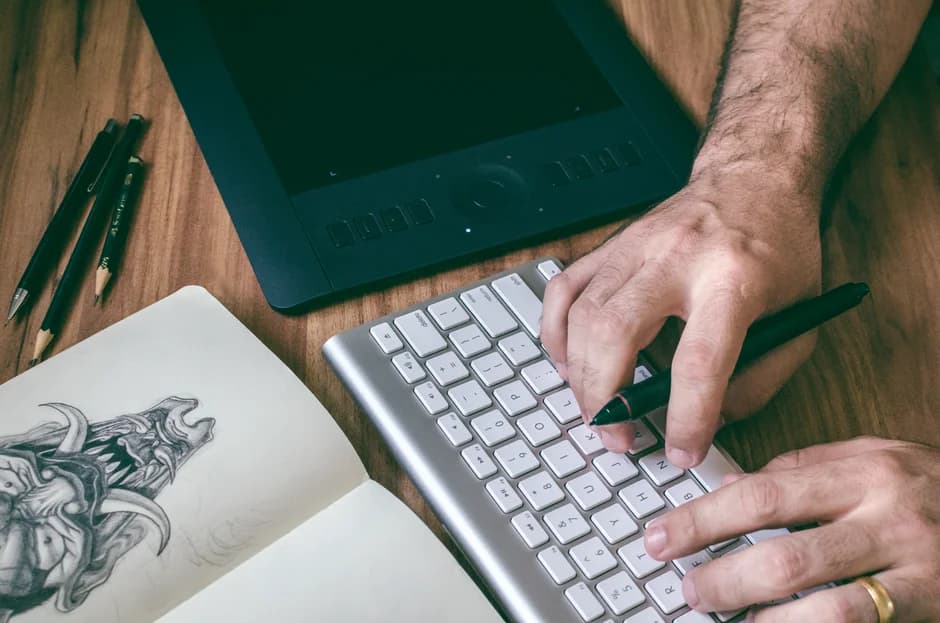 Designer working on a tablet beside a keyboard and sketchbook