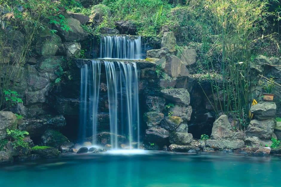 {'role': 'alt_text', 'content': 'Serene waterfall tumbles over mossy boulders in a lush forest near Hangzhou.'}